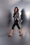 Woman in a black and white patterned top and black pants standing against a reflective gray wall.