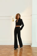 Woman wearing a black outfit with a deep neckline and flared pants in an elegant room.