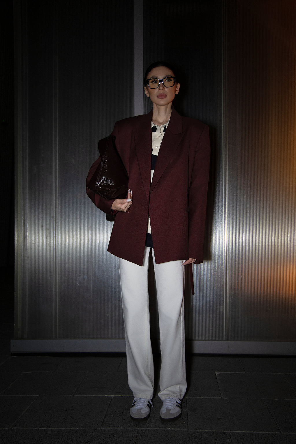Person wearing a burgundy blazer and white pants against a dark background