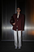 Person wearing a burgundy blazer and white pants against a dark background