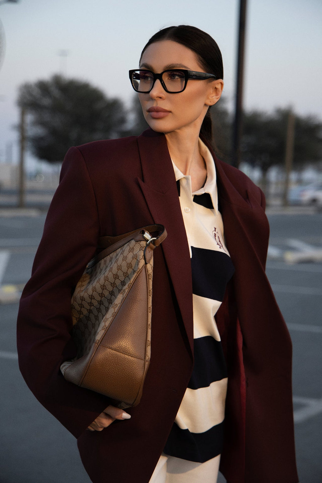 Woman in a burgundy coat holding a brown handbag in an outdoor setting