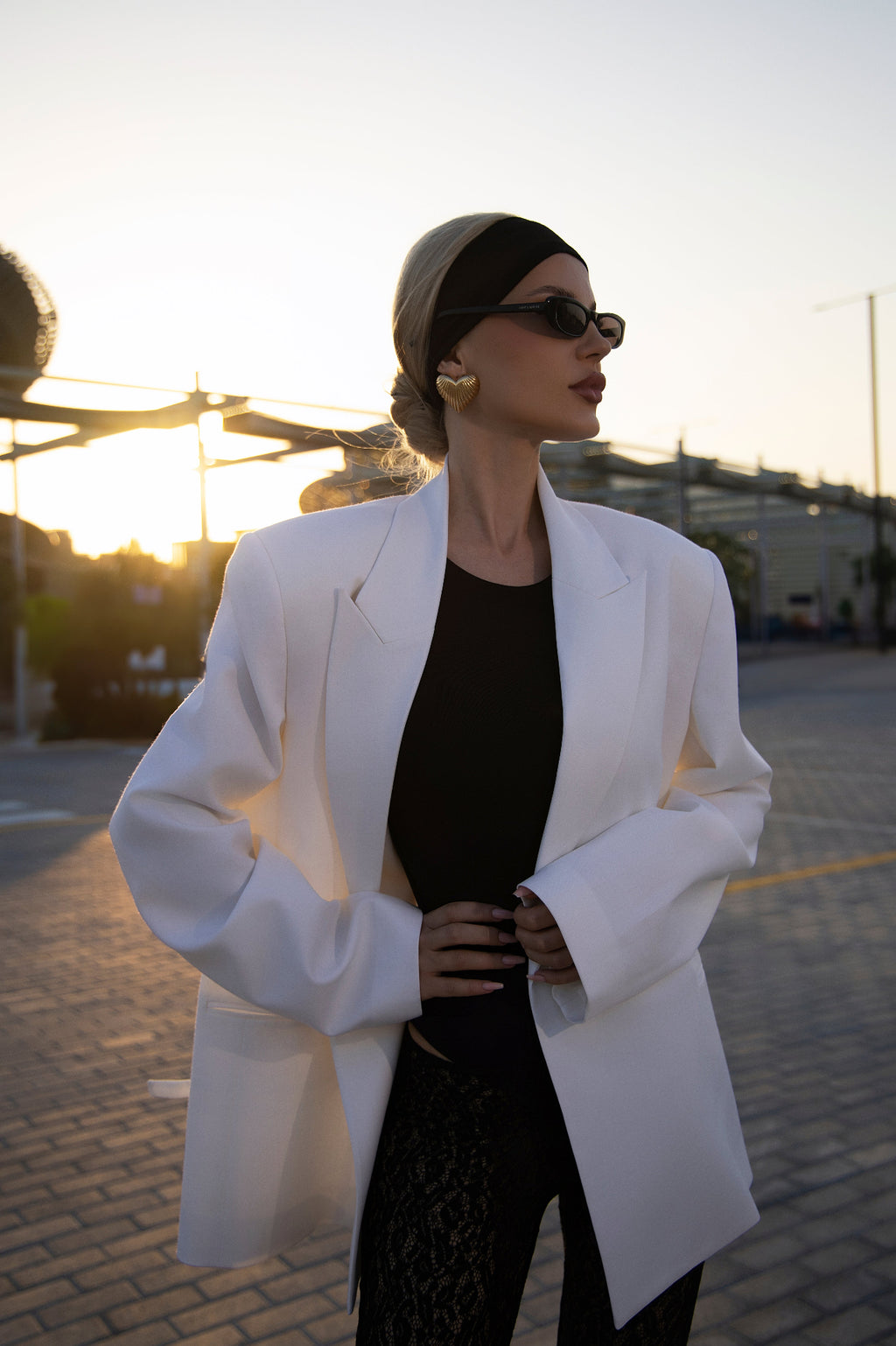 Woman in a white coat and black dress standing outdoors with sunset in the background