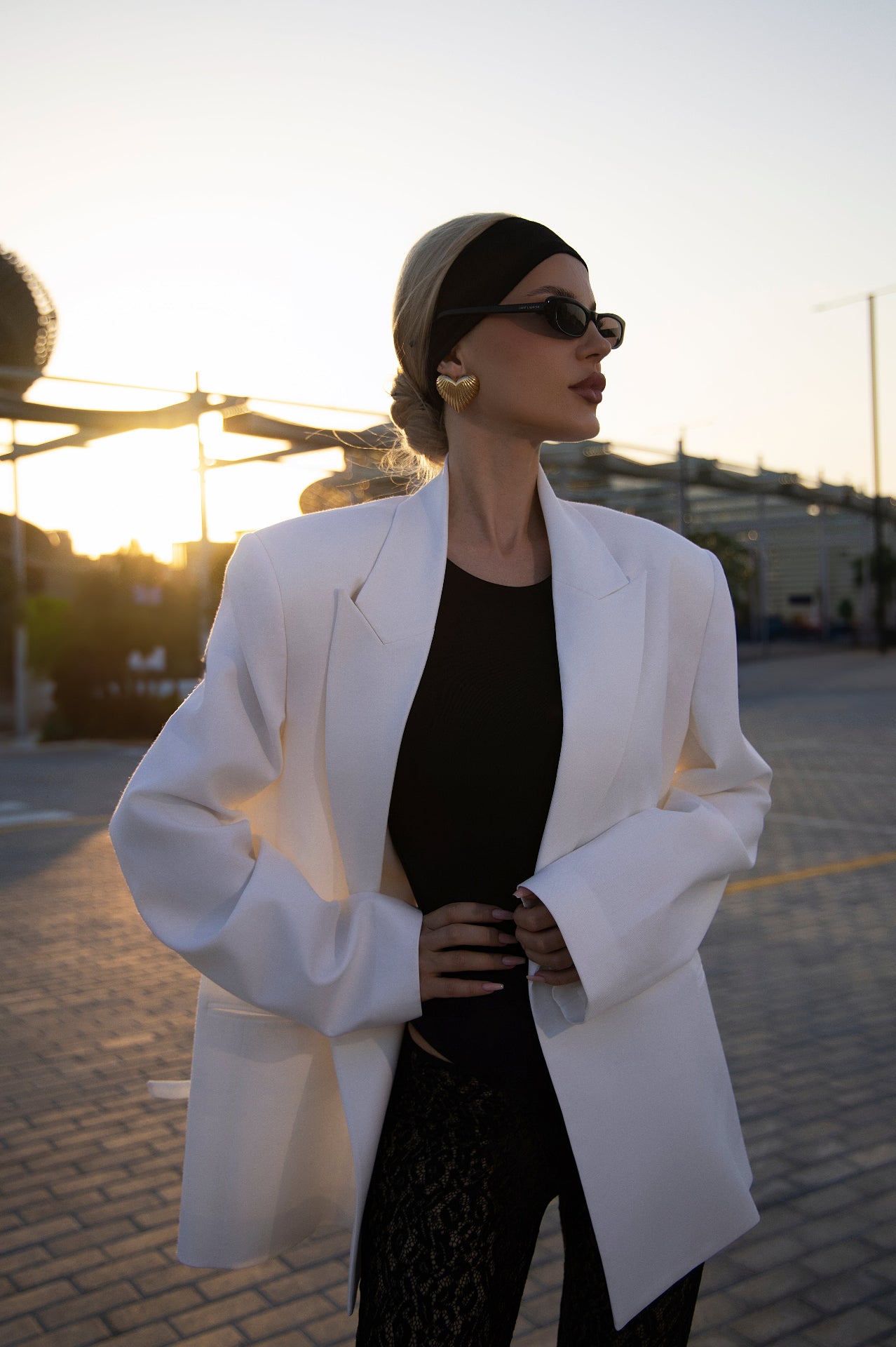 Woman in a white coat and black dress standing outdoors with sunset in the background