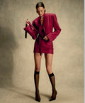 Woman in a burgundy suit holding a matching coat against a beige background