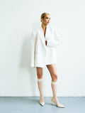Woman in a white outfit standing against a plain background